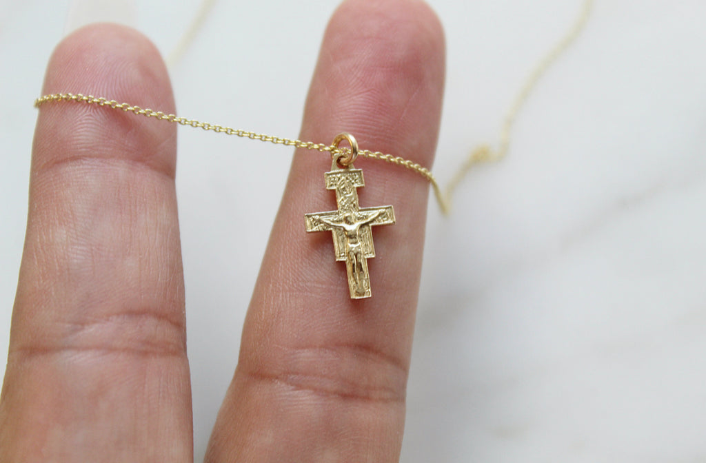 14K Gold San Damiano Crucifix necklace draped over Hand models fingers to show size. Size of Handmade 14K Gold Pendant on the 14K Gold Dainty Chain is 5/8"x3/8".