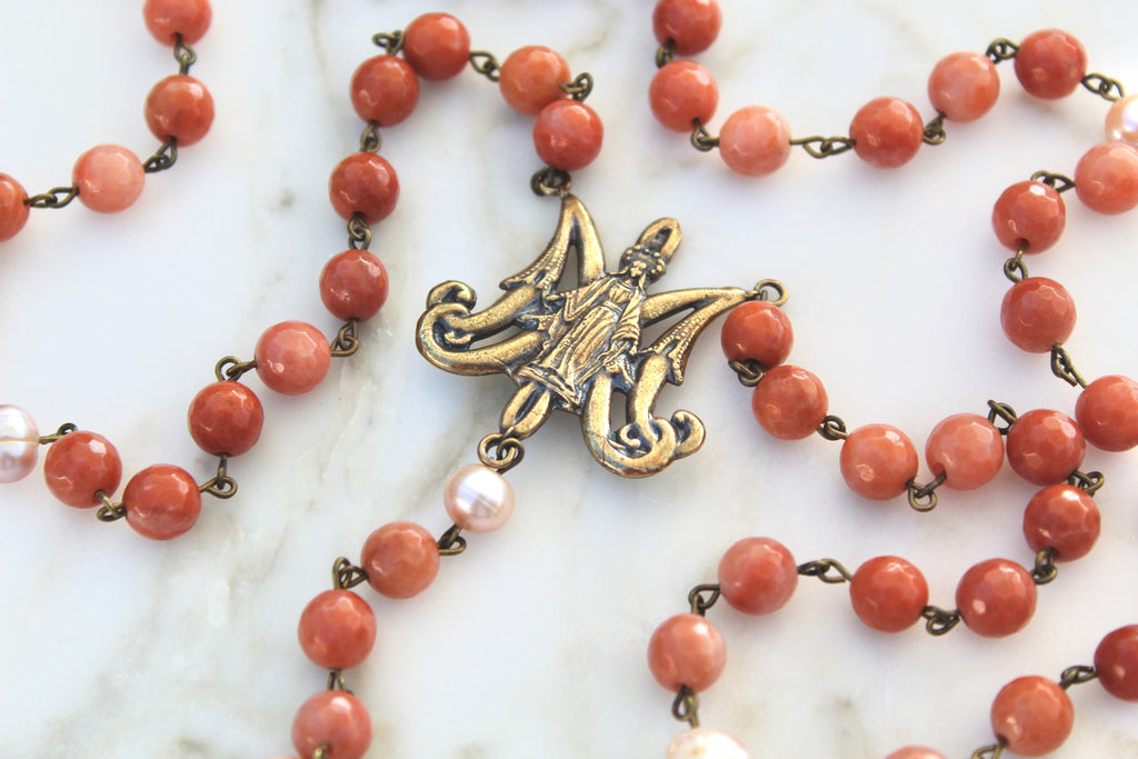 Flat lay photo displaying the Maria Auspice Rosary center, the coral colored stones, and the Pink pearl our fathers.