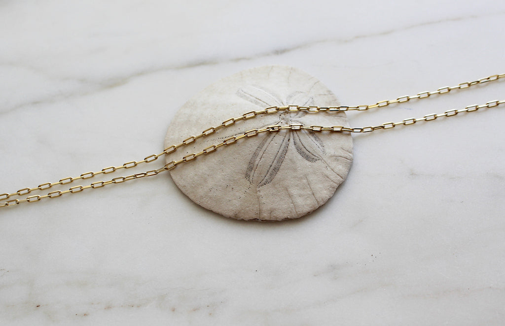 14K Gold Paper Clip Chain Necklace draped over a sand Dollar to show the links.