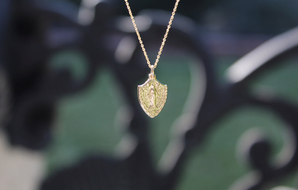 This is a classic Miraculous Medal in 14K Yellow Gold In the shape of a shield. Medal Size on this 14K Yellow Gold Necklace is 9/16" 1/2". The chain on this necklace is dainty and also 14K Yellow Gold.