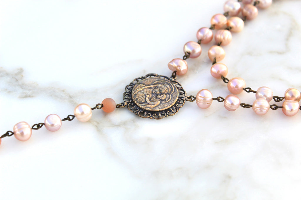 Pink pearl rosary depicts the virgin mary holding baby jesus.