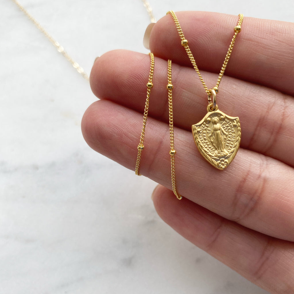 Classic Miraculous Medal Necklace with a little extra because it's shaped like a shield. The Handmade Miraculous medal pendant is 9/16"x1/2". The Necklace is Gold Toned. Medal has classic Miraculous medal Backing with the Marian Cross.