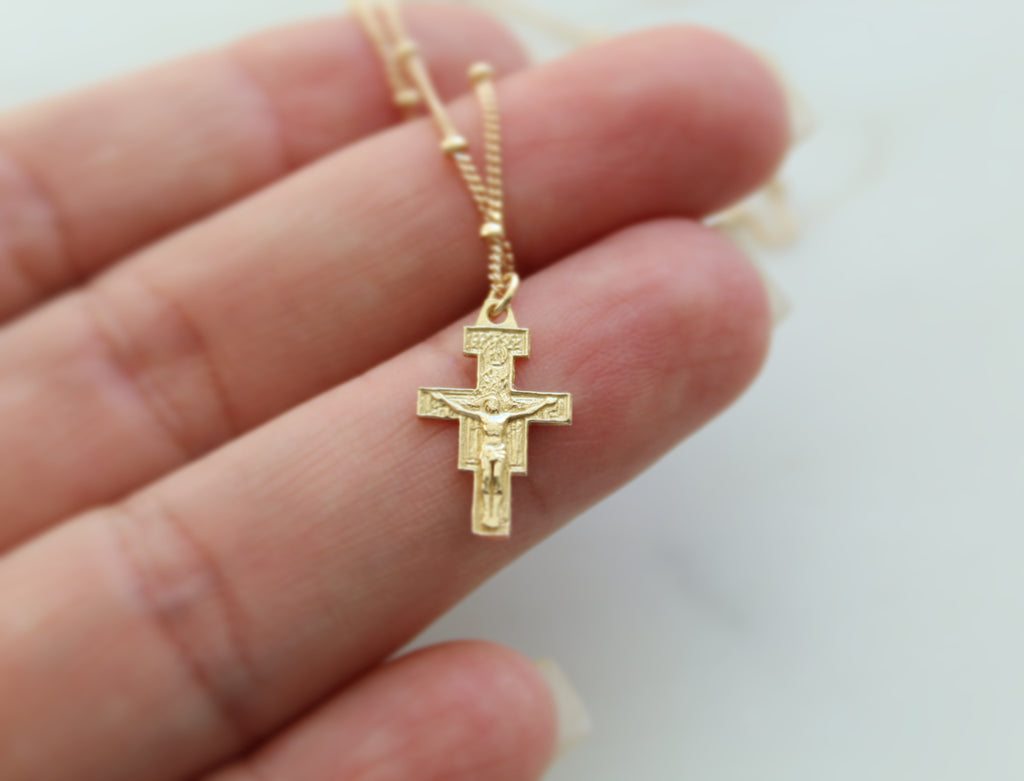 14K Gold San Damiano Crucifix necklace draped over Hand models fingers to show size. Size of Handmade 14K Gold Pendant on the 14K Gold Dainty Chain is 5/8"x3/8".