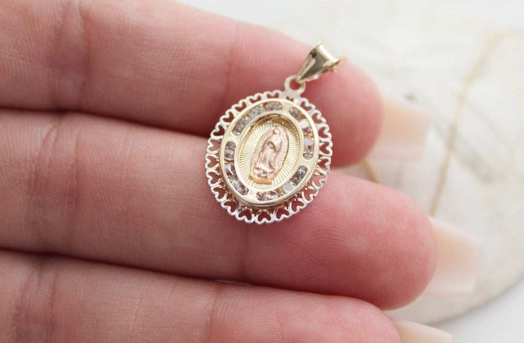 14K Gold Our Lady of Guadalupe necklace. The Guadalupe Pendant has a 14K Rose Gold guadalupe in the center, 14K Yellow Rays surrounding her, 4 curved lines in 14K Yellow Gold that make an cut oval with imbedded Cubic Zirconias, then the outer layer is 14K Gold White Hearts Frame.  Medal is placed over the hand models fingers to show size. 