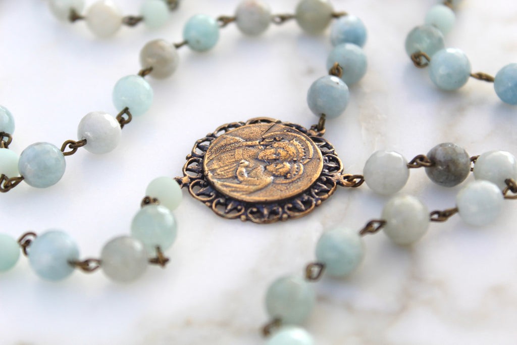 Flat lay photo of the blue stone rosary. Also shows the solid bronze rosary center with baby jesus and mary.