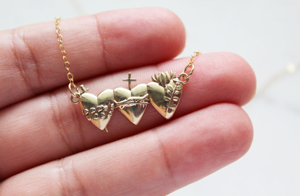 This is the Holy Family Hearts Necklace. Chain is Gold Filled. Medallion is Polished Brass. This necklace has all three of the Sacred Hearts of the Holy Family. Jesus Sacred Heart, Immaculate Heart, & Chase Heart of Joseph. Ethically handmade in Southern California. Medal Size: 1 1/8" x 1/2"
