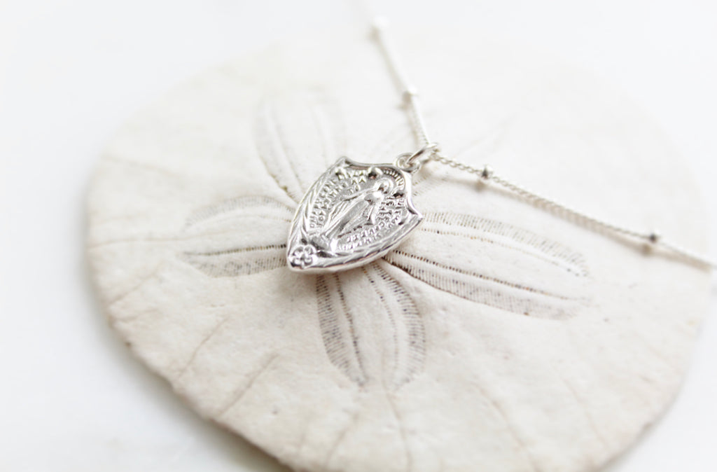 Classic Miraculous Medal Necklace with a little extra because it's shaped like a shield. The Handmade Miraculous medal pendant is 9/16"x1/2". The Necklace is 925 Sterling Silver. Medal has classic Miraculous medal Backing with the Marian Cross.
