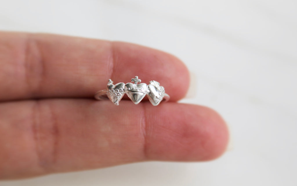 Holy Family Hearts Ring in Sterling Silver. Ring has a simple round band. Ring has the Sacred Heart of Jesus, Immaculate Heart of Mary, chaste heart of st. joseph side by side with the Sacred Heart in the middle. Inside of ring is blank. Markings are expected in all handmade items.