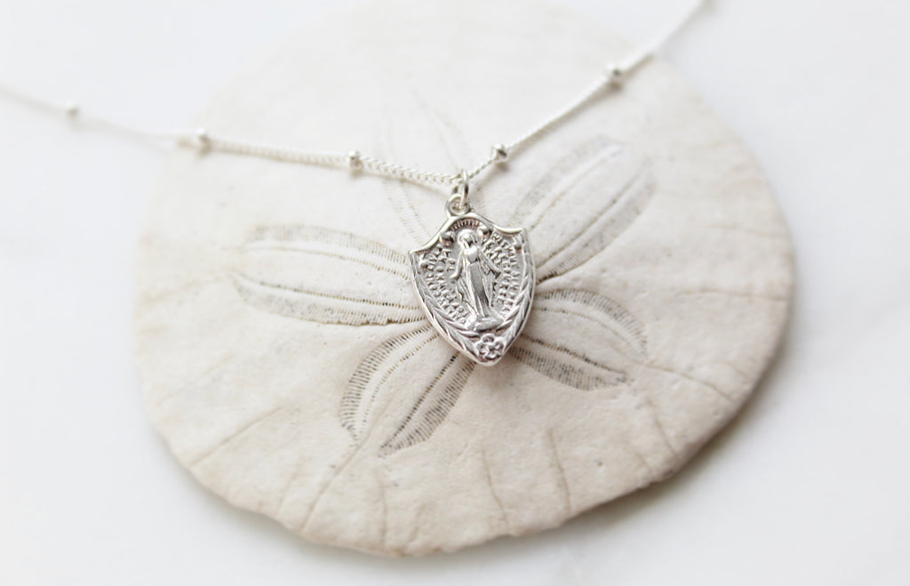 Classic Miraculous Medal Necklace with a little extra because it's shaped like a shield. The Handmade Miraculous medal pendant is 9/16"x1/2". The Necklace is 925 Sterling Silver. Medal has classic Miraculous medal Backing with the Marian Cross.