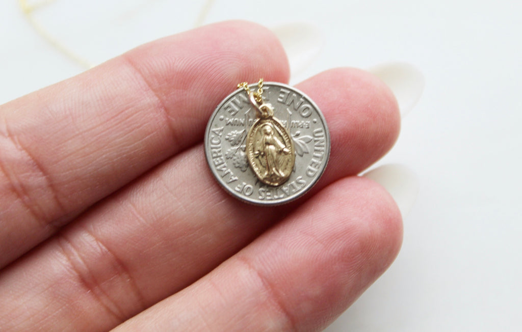 Handmade miraculous medal necklace in 14K Gold. Handmade Miraculous Medal is 1/2"x1/4". Chain is 14K Gold & dainty. This is a traditional miraculous medal with the Marian image on the front and Marian cross & 12 stars on the back. This is a photo of the miraculous medal on a American dime to show the size comparison to the medal.