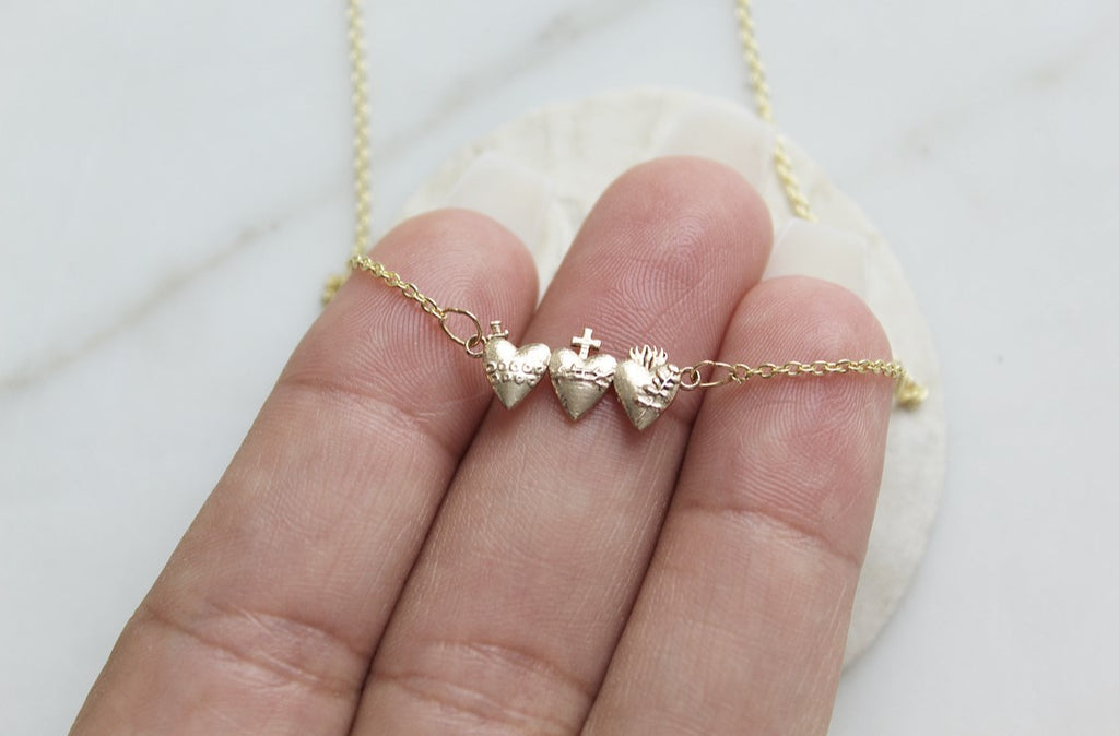 Holy Family Hearts Necklace in 14K yellow Gold. Pendant size: 3/4" X 1/4". Pendant has all three hearts of the Holy family. Chain is a simple and dainty Link style. handmade in southern california. Pendant has hearts side by side: Sacred Heart, Immaculate Heart, Chaste Heart.